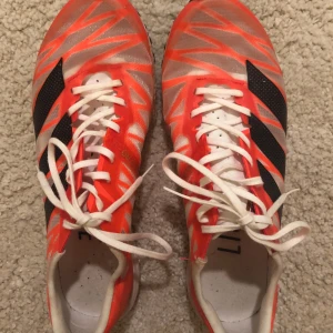 Adidas Adizero Takumi Sen 7 löparskor - Säljer ett par Adidas Adizero Takumi Sen 7 löparskor i en iögonfallande orange färg med svarta och vita detaljer. Skorna har snörning och en lättviktig design, perfekt för löpning.