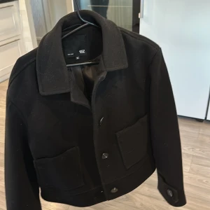 Svart kavaj från 157 - Snygg svart kavaj från 157 med knappar framtill och klassisk krage. Den har en stilren design med två fickor på framsidan. Perfekt för en stilren look.