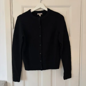 Svart kofta från H&M - Säljer en klassisk svart kofta från H&M med knappar framtill. Den har en rund halsringning och långa ärmar, perfekt för kyligare dagar. Enkel och stilren design som passar till det mesta.