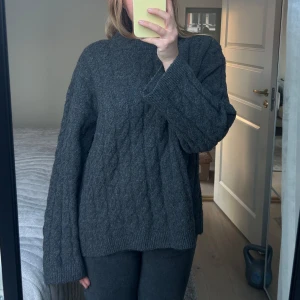 Mörkgrå stickad tröja - Säljer en mysig mörkgrå stickad tröja med kabelstickat mönster. Tröjan har långa ärmar och en avslappnad passform, perfekt för kyliga dagar.