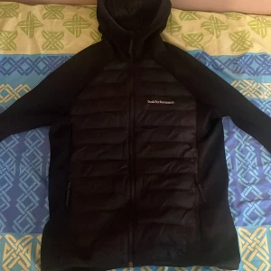 Svart jacka från Peak Performance - Snygg svart jacka från Peak Performance med huva och dragkedja. Jackan kan användas av både tjejer och killar och köptes under black friday så har knappt blivit använd. Är storlek L men är väldigt liten av sig så kan användas för folk med M också. Köptes för 1100 kr.