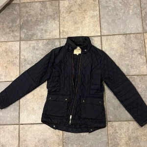 Svart quiltad jacka från Boomerang - Säljer en snygg svart quiltad jacka från Boomerang i storlek M. Jackan har långa ärmar och praktiska fickor med knappar. Perfekt för höst och vår, med en stilren design och dragkedja framtill. Passar både till vardags och lite finare tillfällen.