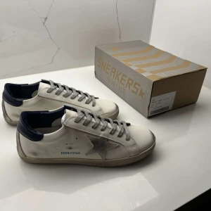 Golden goose superstar - ✨ Golden Goose Sneakers ✨ Upplev en perfekt mix av stil och komfort med dessa vita sneakers med blå detaljer från Golden Goose. 👟💙 Deras ikoniska, lätt slitna design ger en avslappnad och trendig look som passar både vardag och fest. ⭐ Med högkvalitativa material och handgjorda detaljer är de skapade för dig som älskar exklusivitet och edge. 🔥  Ett måste i garderoben för den som vill sticka ut med stil! 🕶️✅                                      Vid snabb och smidig affär kan priset diskuteras!🤝