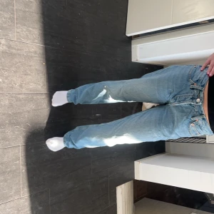 Blå jeans - Säljer ett par klassiska blå jeansbyxor i mycket bra skick. De har en normal passform och är perfekta för vardagsbruk. Byxorna har en traditionell femficksdesign och stängs med dragkedja och knapp. Perfekta för både vår och höst!