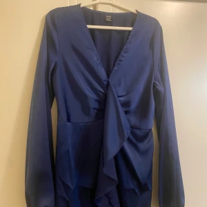 Mörkblå långklänning från Shein - Säljer en elegant mörkblå långklänning från Shein. Klänningen har långa ärmar och en v-ringad omlott-design med volangdetaljer framtill. Perfekt för höst- och vinterfester! 💙