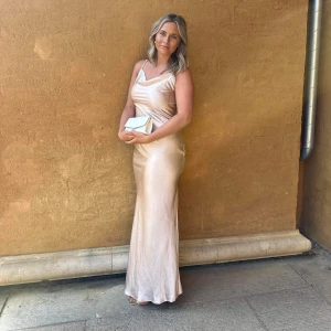 Balklänning  - Elegant champagnefärgad långklänning i siden med en vacker drapering över bysten. Klänningen har en smickrande passform och är perfekt för festliga tillfällen. Den axelbandslösa designen ger en sofistikerad look. Hade den på min bal och den funkade perfekt för de❤️