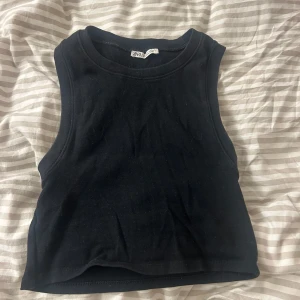 Svart ärmlös topp från Zara - Säljer en stilren svart ärmlös topp från Zara i storlek S. Perfekt för sommardagar eller som ett basplagg i garderoben. Toppen är i bra skick och gjord av mjukt material för en bekväm passform.