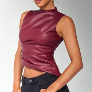 Vinröd ärmlös topp i skinnimitation - Snygg vinröd ärmlös topp i skinnimitation med hög hals och dragkedja i ryggen. Perfekt för en trendig look.