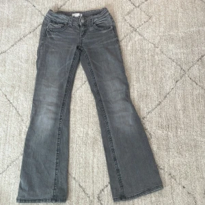 Grå bootcut jeans från Gina Tricot - Snygga grå bootcut jeans från Gina Tricot i storlek 146. De har en klassisk femficksdesign och knappgylf. Perfekta för en avslappnad stil med en touch av retro.