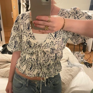 Vit och blå blus med knytning - Säljer en superfin vit blus med blått blommönster. Den har korta ärmar och en söt knytning framtill som ger en fin passform. Pris kan diskuteras☺️