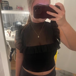 Svart topp med volangdetaljer - Snygg svart topp med volangdetaljer på axlarna. Toppen är perfekt för en kväll ute eller ett sammanhang man vill känna sig extra fin!! Pris kan diskuteras🥰