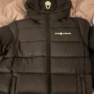 Svart dunjacka från Sail Racing - Säljer en svart dunjacka från Sail Racing i mycket bra skick. Jackan har en dragkedja framtill och är perfekt för kyliga dagar. Den är långärmad och har en stilren design med logotypen på bröstet. Perfekt för både vardag och utomhusaktiviteter! Passar både S/M, pris går att diskuteras!