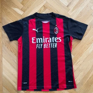 AC Milan fotbollströja - Säljer en AC Milan fotbollströja i rött och svart med klassiska ränder. Tröjan är kortärmad och har Puma-loggan på bröstet samt 'Emirates Fly Better'.  🖤❤️