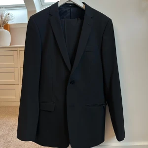 Svart kavaj tiger of Sweden  - Snygg svart kavaj i klassisk stil. Perfekt för både formella och semi-formella tillfällen. Kavajen har en enkel knäppning med två knappar och fickor fram. Passar bra till både byxor och jeans för en stilren look.
