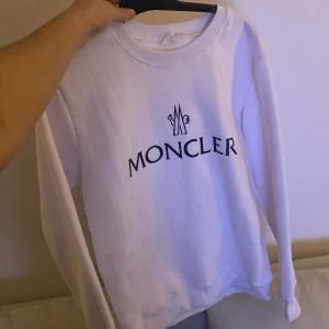 Vit Moncler - Säljer en snygg vit tröja från Moncler i mycket bra skick. Den har en klassisk rund hals och långa ärmar. Perfekt för både vardag och lite finare tillfällen. Moncler-loggan är tryckt i svart på framsidan. 