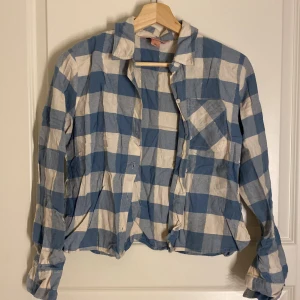 Blå och vit rutig skjorta - Säljer en blå och vit rutig skjorta med långa ärmar och knappar framtill. Skönt material, från hunkemöller