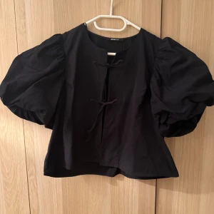 Svart blus från Gina Tricot - Superfin svart topp från Gina Tricot med puffiga ärmar och knytning framtill! Är i storlek L men passar S-L, superfint skick🖤