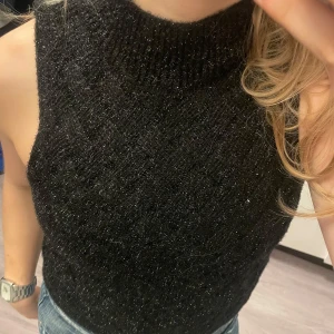 Svart glittrig ärmlös topp från Mango - Snygg svart glittrig topp från Mango i storlek XS. Den är ärmlös och har en hög hals. Toppen är ny med taggar kvar.