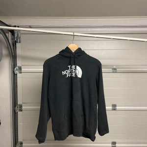 Svart hoodie från The North Face - Säljer en svart hoodie från The North Face i bra skick. Den har en stor logga på framsidan och en praktisk känguruficka. Perfekt för kyliga dagar eller som ett extra lager. Passar både till vardags och för utomhusaktiviteter. Hör av dig vid intresse! Säljes i befintligt skick. Storlek: XL