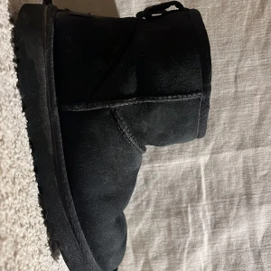 Svarta boots från UGG - Säljer ett par svarta UGG-boots i ok skick. De är gjorda av mocka och har en klassisk design med rund tå och mjuk insida. Perfekta för höst och vinter för att hålla fötterna varma och bekväma. Passar till både vardag och mer avslappnade tillfällen. Som man ser är dom slitna men är fof i bra skick och går att använda bra