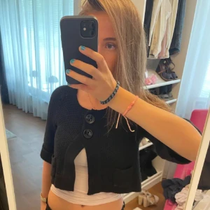 Svart stickad kofta med stora knappar - Säljer en svart stickad kofta med trekvartsärm och stora knappar framtill. Den har en croppad passform och två små fickor fram. Funkar både till vardags och fest. Superfin att matcha med en enkel topp under!