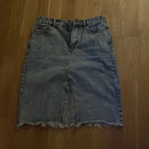 Jeanskjol med liten slits - Säljer en cool jeanskjol i klassisk blå med rå kant och slits framtill. Kjolen har en vintage look och knappstängning. Perfekt för en avslappnad stil eller festivaloutfit! 🕶️