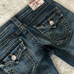 Blå vintage jeans från True Religion - Säljer ett par skiiiit snygga blå vintage jeans med SUPER låg midja från True Religion i storlek 24. Dom är vintage och går därför inte att få tag i någon Annan stans(därav kommer priset) jag köpte dom för 2300kr. Jag säljer dom då jag inte tycker att de passar min stil och jag har de 4-5 gånger tror jag.💞💞de har inga defekter utan bara ”slitningarl” i byxan men det är där från början alltså det var så byxorna var gjorda😊jag är 165cm om någon vill veta🤗Innerbenslängden är 82cm och midjemåttet är