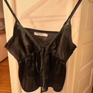 Svart satinlinne från NA-KD - Snyggt svart satinlinne från NA-KD i storlek XS. Linnet har smala axelband och fina spetsdetaljer längs kanten. Perfekt för en utekväll eller fest! 💫