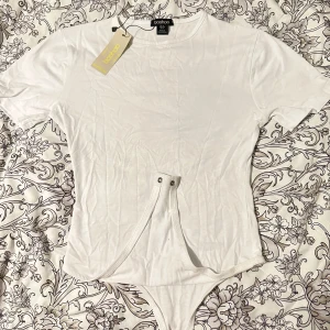 Vit bodysuit T-shirt - Boohoo - Säljer min vita bodysuit köpt från Boohoo med prislappen fortfarande kvar. Den är oanvänd 💞 