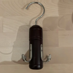 Praktisk bälteshängare i mörkt trä - Säljer en smidig bälteshängare i mörkt trä med metallkrokar. Perfekt för att organisera dina bälten i garderoben. Den har en stilren design och är enkel att hänga upp. Passar bra för att hålla ordning och spara plats. Perfekt för alla som vill ha en snygg och praktisk lösning för sina accessoarer.