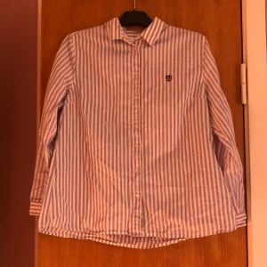 Randig skjorta från Bondelid  - Säljer en stilren och klassisk randig skjorta från Bondelid i storlek 44. Skjortan är lila och vit med långa ärmar och knappar framtill. Perfekt för både vardag och festliga tillfällen. Regular fit för en bekväm passform. Passar bra till både jeans och chinos!