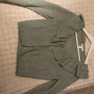 Stickad tröja från hm - Stickad tröja från hm, med kanappar hela vägen, och volanger upptill m