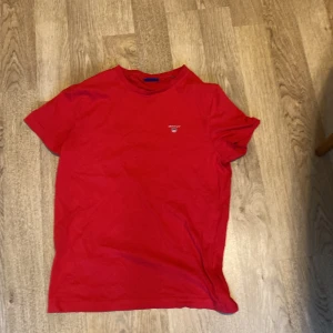 Röd t-shirt från GANT - Säljer en snygg röd t-shirt från GANT passar i storlek S och M. Den är kortärmad och gjord av mjuk bomull. T-shirten har en liten logga på bröstet och är i nyskick. Passar både till vardags och festliga tillfällen. Skicka ett meddelande vid intresse! 🔥