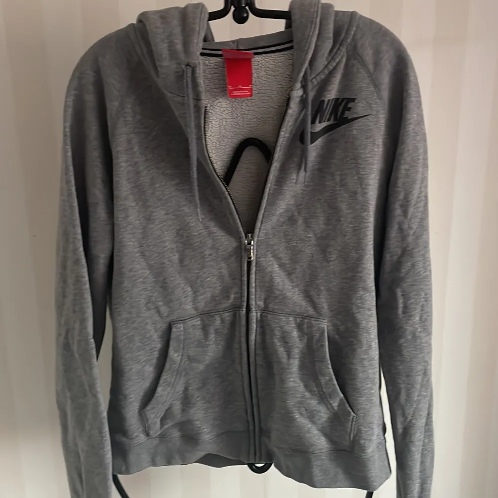 Säljer en grå hoodie från Nike i storlek M. Den har en dragkedja framtill och en klassisk Nike-logga på bröstet. Perfekt för både träning och vardag. Den är i bra skick och superbekväm att ha på sig. Passar perfekt till höst och vår!. Hoodies.