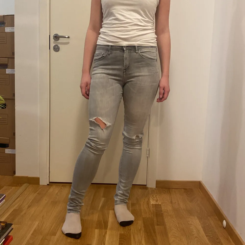 Säljer ett par grå skinny jeans i storlek 28x34. De har en snygg slitning på ena knät och är perfekta för en casual look. Jeansen är i bra skick och passar till både vardag och fest. Sköna och stretchiga för bästa komfort!. Jeans & Byxor.