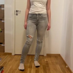 Grå skinny jeans - Säljer ett par grå skinny jeans i storlek 28x34. De har en snygg slitning på ena knät och är perfekta för en casual look. Jeansen är i bra skick och passar till både vardag och fest. Sköna och stretchiga för bästa komfort!