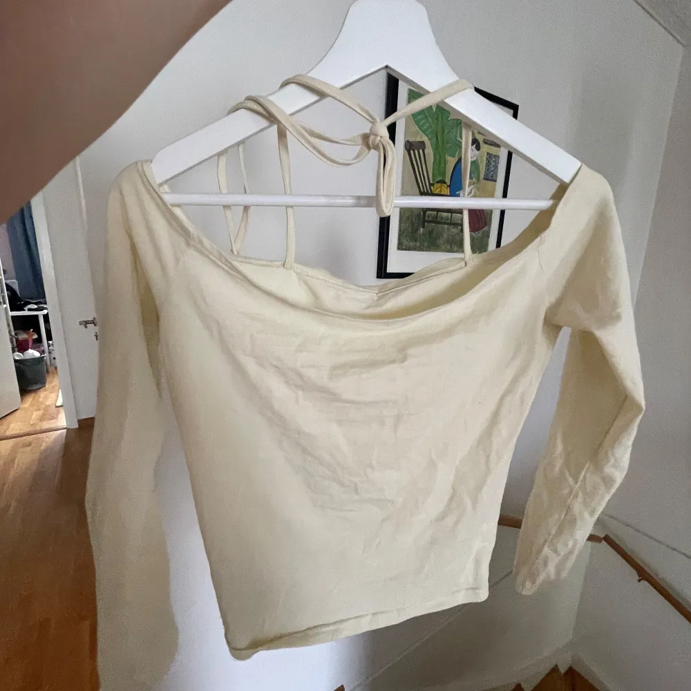 Säljer en snygg beige offshoulder topp med långa ärmar. Toppen har en stilren design med knytband i ryggen för en extra detalj. Perfekt för både vardag och fest!. Toppar.