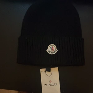Svart Moncler Mössa - Säljer en snygg svart Moncler mössa den är helt oanvänd 