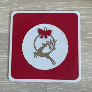 Handgjort julkort med ren och pingvin - Detta är ett superfint handgjort julkort med en ren i en cirkel och en röd rosett på framsidan. Inuti finns plats för att skriva en hälsning, dekorerat med en söt pingvin och hjärtan. Baksidan har ett vackert rött hjärta med spetsdetaljer. Perfekt för att sprida julglädje! 🎄❤️