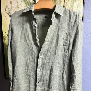 Grön linneskjorta från Zara - Säljer en stilren grå linneskjorta från Zara. Perfekt för både vardag och fest! Skjortan har långa ärmar och knappar framtill. Materialet är lätt och luftigt, vilket gör den idealisk för vår och sommar. Passar bra till både jeans och chinos. Hör av dig vid intresse! 😊