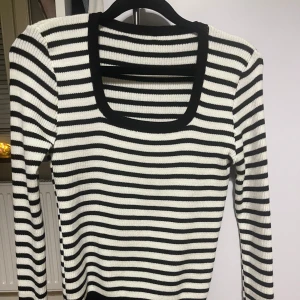 Randig ribbad tröja - Säljer en helt ny randig tröja i svart och vit. Den är ribbad och har en fyrkantig halsringning som ger en snygg touch. Perfekt för vardag! Tröjan har långa ärmar och är gjord av ett mjukt och stretchigt material som sitter bekvämt. Aldrig använd, så den är i perfekt skick!