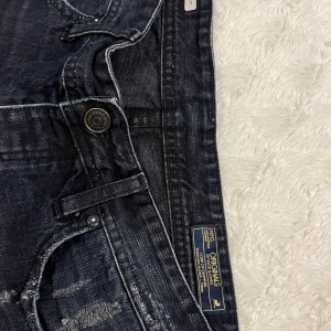 Mörkblå jeansshorts från Jack & Jones - Säljer ett par snygga mörkblå jeansshorts från Jack & Jones i storlek L. De har en cool slitningseffekt och knappar i midjan. Perfekta för en avslappnad sommarlook. Passar bra till både t-shirt och skjorta!