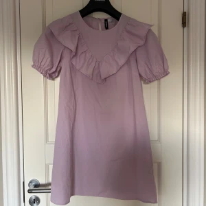 Ljuslila klänning med volangdetaljer - Säljer en söt ljuslila klänning med volangdetaljer runt halsen och korta puffärmar som tyvärr inte kommer till användning 💜