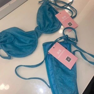 Blå glittrig bikini med knytband - Säljer en superfin blå glittrig bikini. Den har knytband i ryggen. Underdelen är i storlek s typ och överdelen i M typ, passar mig som har 75C i bh storlek men kupan går att göra större och mindre. Aldrig använd lapparna sitter kvar på båda delarna priset går att diskutera💙💕trosan är string och man knyter den i sidorna 