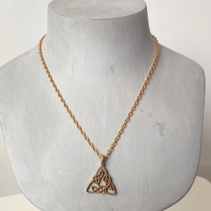 Guldhalsband med keltisk knut - Säljer ett elegant guldhalsband med en vacker keltisk knut som hänge. Kedjan är tunn och smidig, perfekt för både vardag och fest. Hänget har en intrikat design som ger en mystisk och tidlös känsla. Passar perfekt som en unik accessoar eller en speciell present.