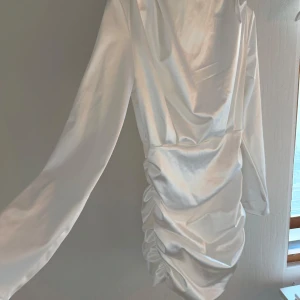 Satin klänning - Elegant vit klänning i satin med långa ärmar och draperad design. Perfekt för en stilren look med en touch av glamour. Passar perfekt till studenten!!
