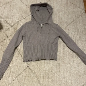 Grå croppad hoodie med dragkedja - Säljer en stilren grå croppad hoodie med dragkedja och huva. Tröjan har långa ärmar och en ribbad nederkant som ger en snygg passform. Perfekt för en avslappnad look. Diskuterar gärna pris💗XXS XS är storleken💕Den kommer från Gina tricot 💗