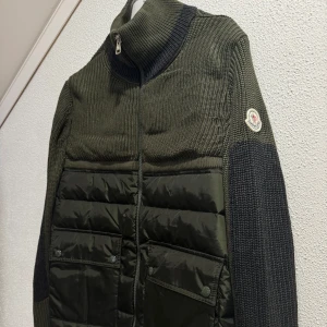 Grön stickad jacka från Moncler - Snygg grön stickad jacka från Moncler med quiltade detaljer och dragkedja framtill. Jackan har en hög krage och Moncler-logga på ärmen. Perfekt för kyligare dagar med sin stilrena design och praktiska fickor.      Storlek M-L     NFC-Scan finns.  Bortslarvat kvitto!