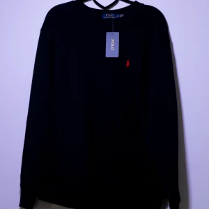 Ralph Lauren sweatshirt - Säljer en stilren svart tröja från Ralph Lauren med det klassiska röda logotypbroderiet på bröstet. Tröjan har långa ärmar och en rund halsringning. Perfekt för en avslappnad och elegant look.