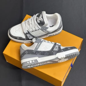 Grå och vita sneakers från Louis Vuitton - Stilrena sneakers i grått och vitt med klassiskt Louis Vuitton-mönster. Skorna har snörning och en bekväm sula, perfekt för en trendig look. Detaljerna inkluderar märkets logotyp på tungan och sidan.